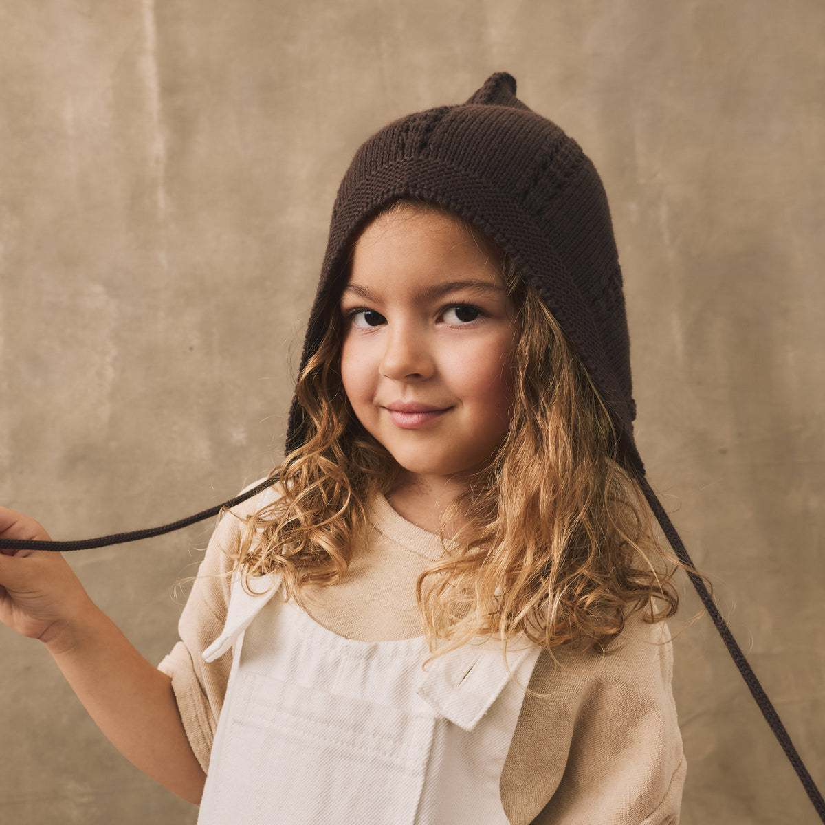 Girl in a brown knit gnome hat and cream dungarees, The Simple Folk