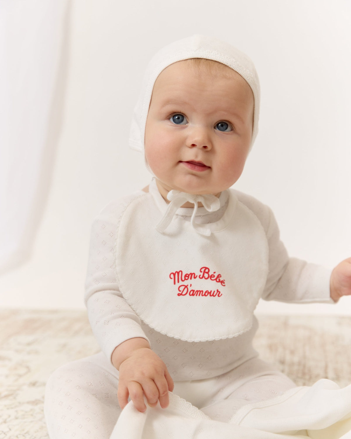 Baby in a white bonnet and Mon Bebe footie, KIPP